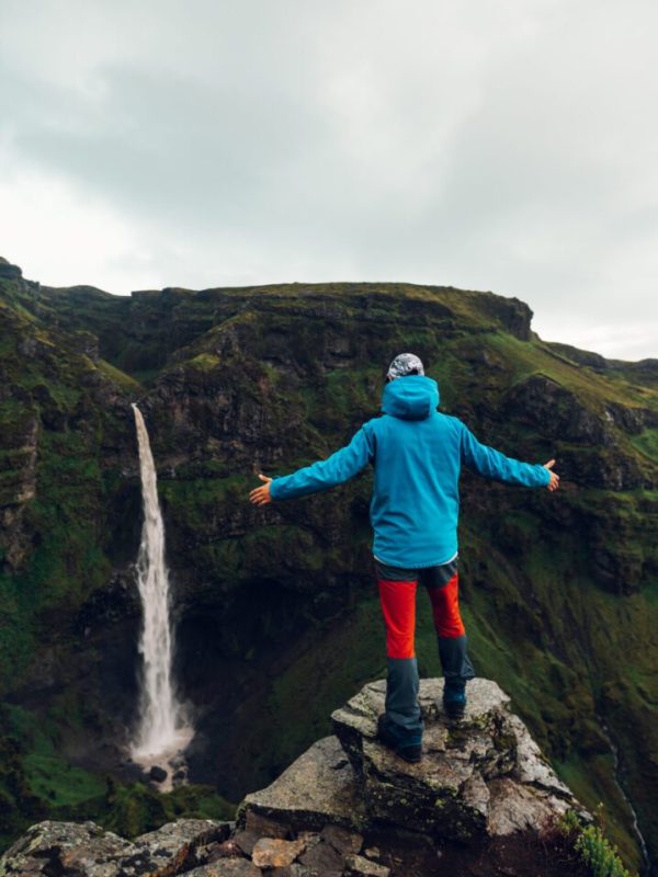An explorer in the wild nature of Iceland. A man on a cliff is watching the waterfall in the wild nature of Iceland. A man is discovering beauty in nature in the mountains.